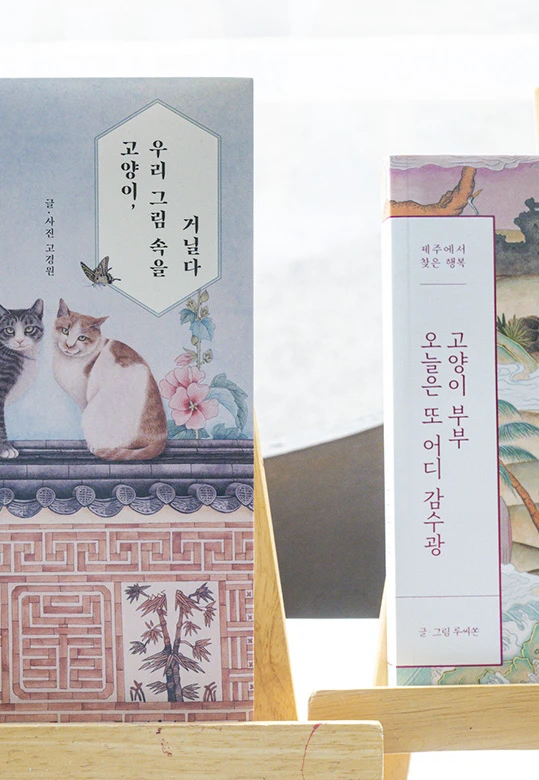 나무 이젤에 세워진 루씨손 작가의 에세이, 고양이와 한옥 담장을 그린 민화풍 표지가 돋보이는 모습