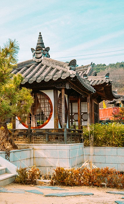 둥근 창이 있는 기와 정자, 푸른 하늘 아래 소나무와 어우러진 서동요 촬영지의 한옥 풍경