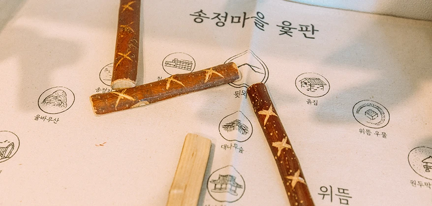 송정마을 윷판이라 적힌 종이 위에 직접 만든 나무 윷가락이 놓이고, 마을 명소가 그림으로 표시돼 있다