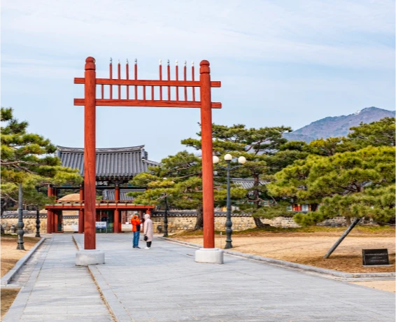 수로왕릉 진입로의 붉은 홍살문과 그 너머 기와 정문, 소나무 사이를 걷는 사람들