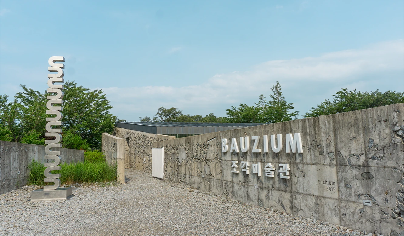 콘크리트 담벼락에 BAUZIUM 조각미술관 글자가 새겨진 바우지움 입구와 철제 사인