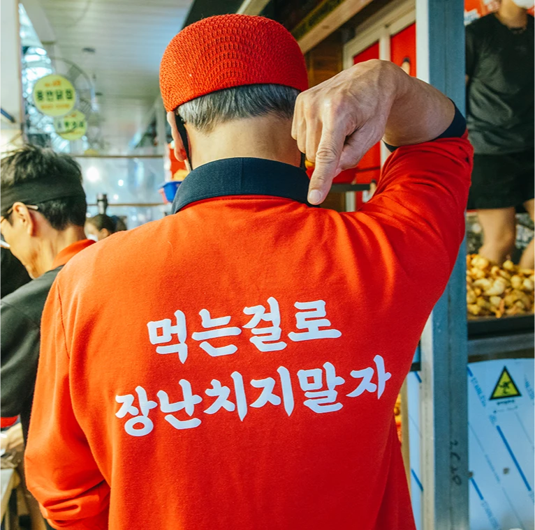 먹는 걸로 장난치지 말자 문구가 적힌 주황색 티셔츠를 입은 상인의 뒷모습