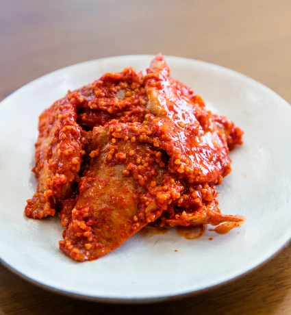 흰 접시 위에 붉은 양념이 자작하게 밴 완성된 가자미식해가 먹음직스럽게 클로즈업된 모습