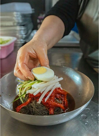 양은 그릇에 담은 명태회냉면 위에 삶은 달걀 반쪽을 올리는 주방의 손길