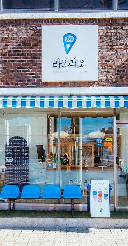 벽돌 외벽과 파란 줄무늬 차양이 돋보이는 속초 젤라또 가게 라또래요의 외관