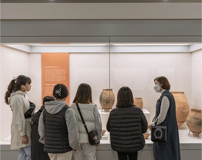 유리 진열장 안 백제 토기들을 관람객들이 둘러서서 해설을 들으며 감상하는 모습