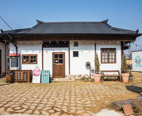맑은 하늘 아래 기와지붕 농가를 개조한 카페의 외관과 마당에 놓인 메뉴판과 벤치