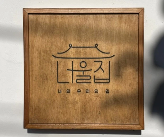 기와 지붕을 형상화한 한글 로고가 새겨진 너울집의 원목 간판
