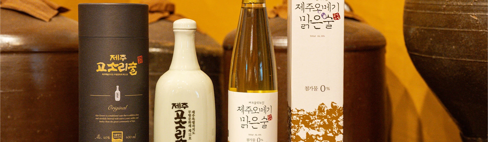 고소리술, 막걸리 등 제주 전통주 네 병이 옹기 항아리를 배경으로 나란히 놓인 모습